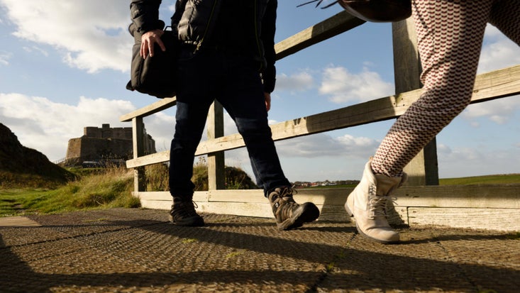 Two pairs of legs crossing a bridge with Lindisfarne Castle in the background